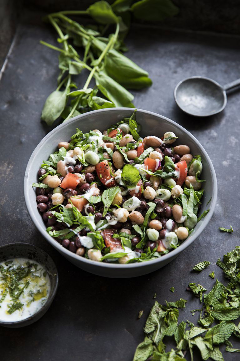 Four-bean salad with beef tomato and watercress in a bowl with basil on the side.