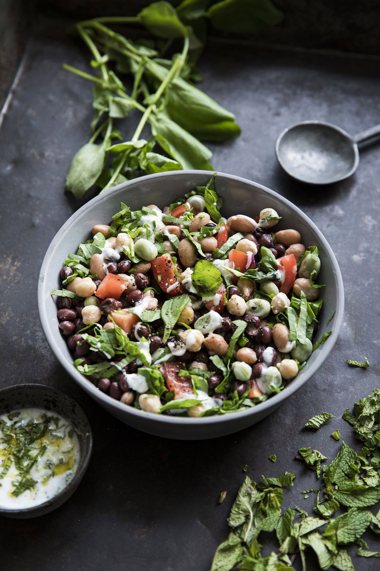 Vierbonensalade met vleestomaat en waterkers in een kom met basilicum er naast.