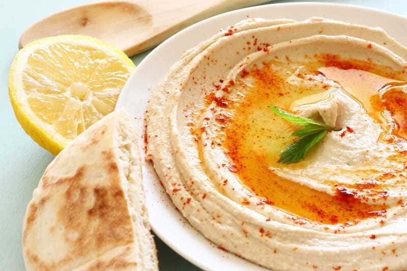 Hummus in white bowl with cayenne pepper, olive oil and lemon. 