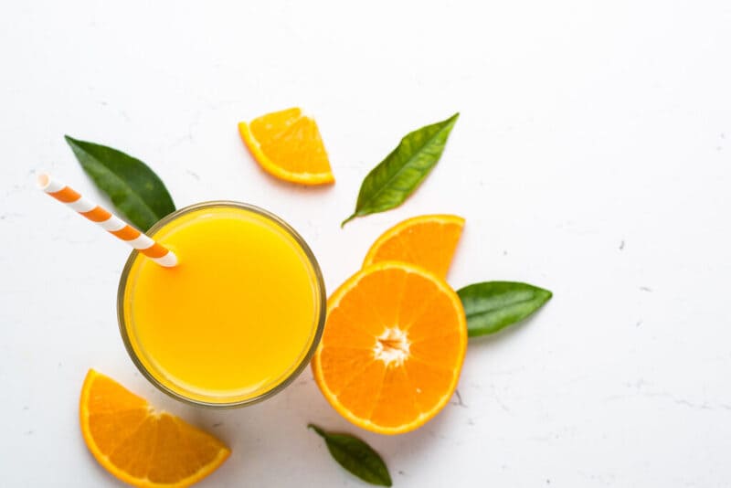 Tropische sinaasappelsap in een glas met een rietje en sinaasappels aan de zijkant.