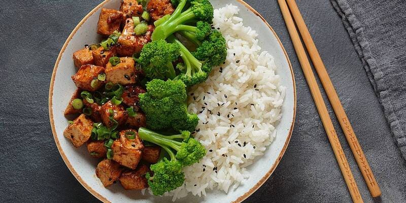 Plate with rice, broccoli, and tempeh with chopsticks on the side.