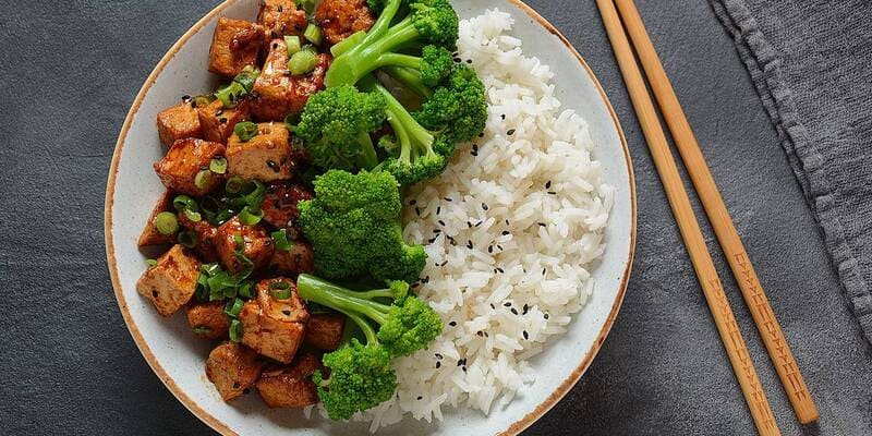 Bord met rijst, brocolli en tempeh en stokjes er naast.