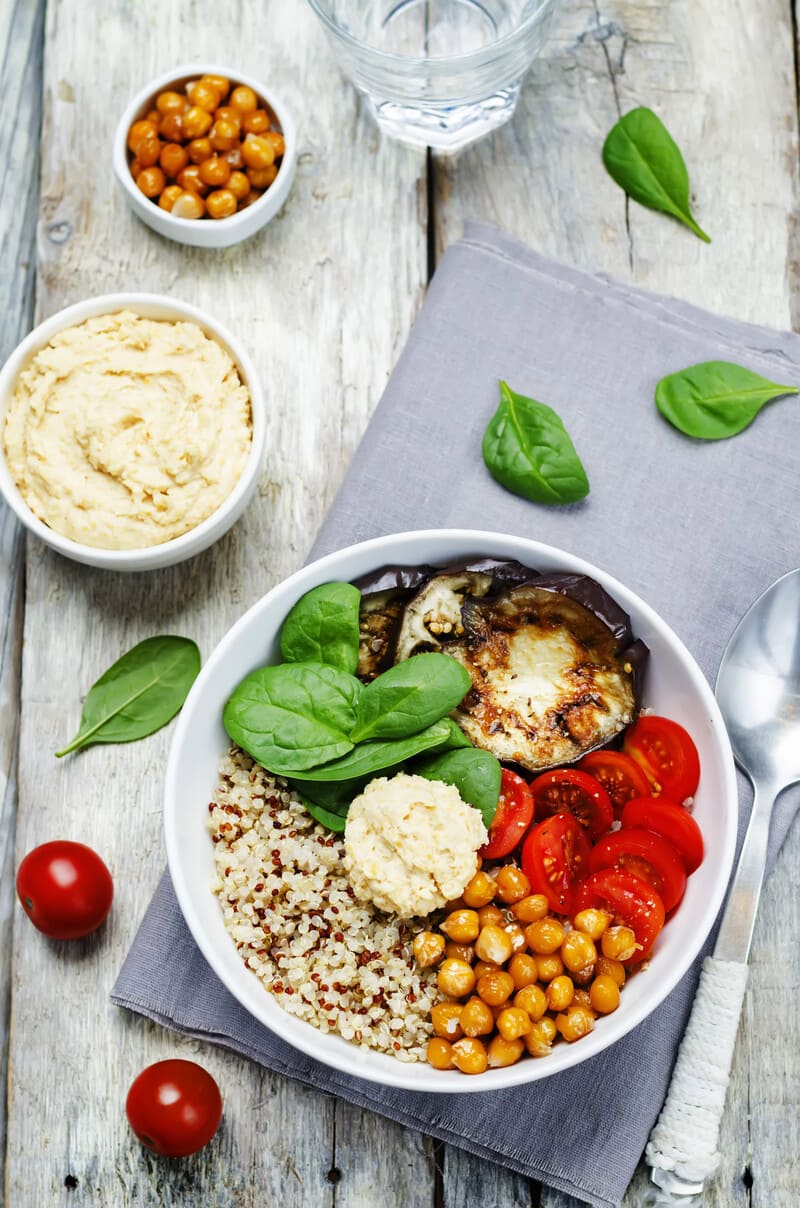 Vegan mezze plate met aubergine, tomaat, kikkererwten, spinazie en quinoa geserveerd in een witte kom.