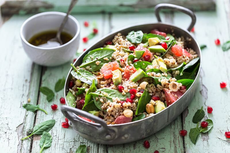 Large bowl of quinoa salad with baby spinach, avocado, chickpeas, and tomato.