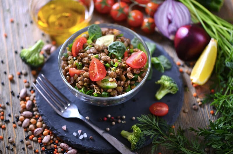 Lentil spinach salad served in a bowl with tomatoes and vegetables in the background.