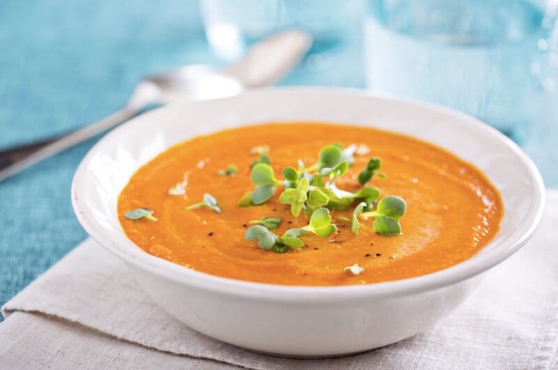 Orange soup in a white bowl with garnish and black pepper. 