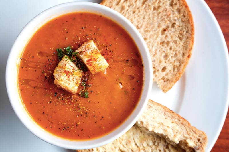 Tomato soup with croutons in a white bowl, served with bread on the side.