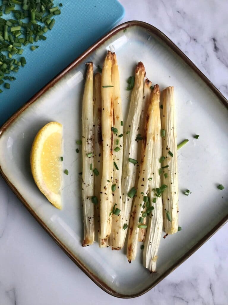 Beautiful square plate with asparagus adorned with chives and lemon.