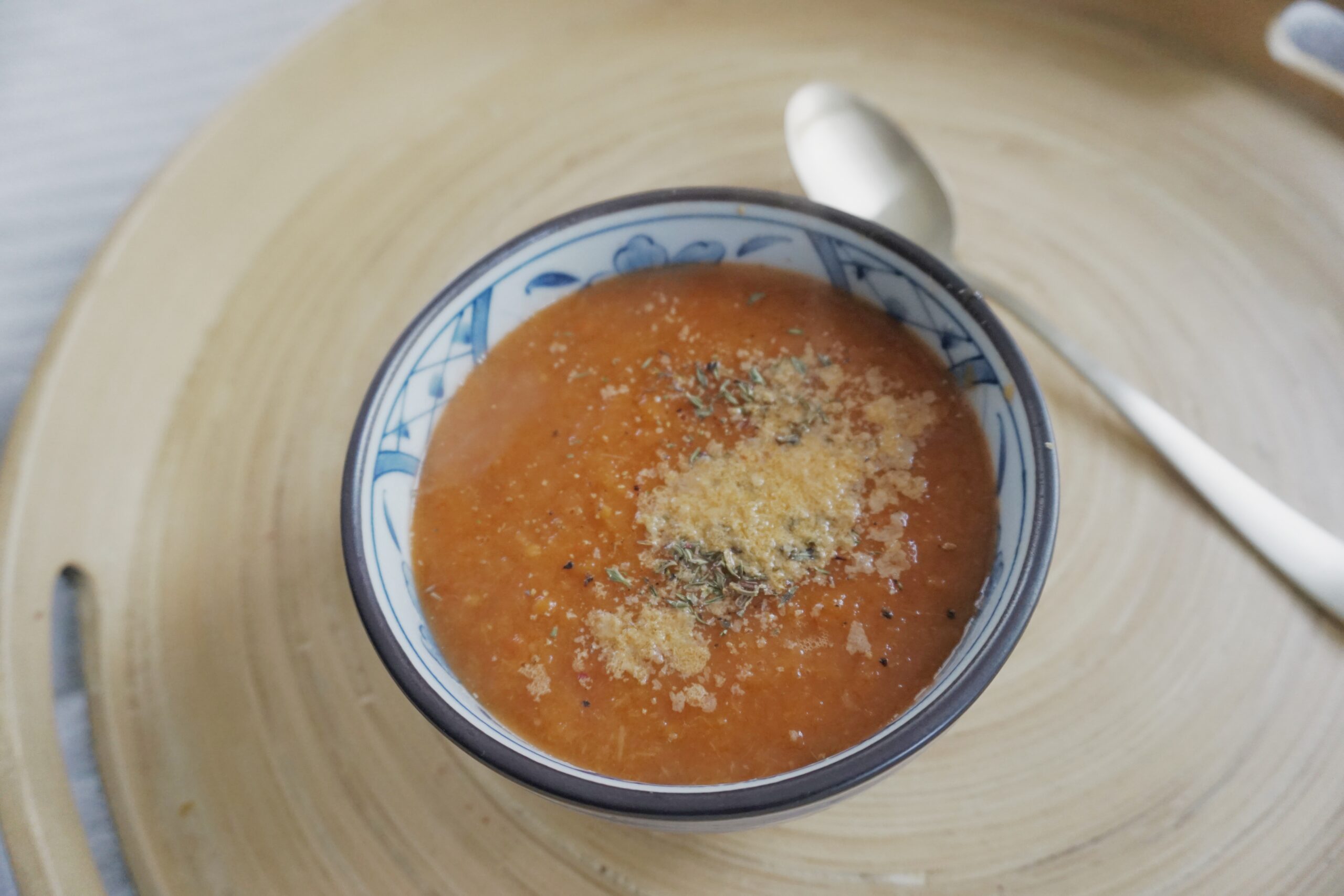 Tomato and fennel soup in a bowl with herbs on a wooden plate.