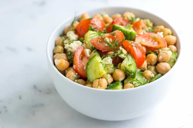 Chickpea salad in a white bowl with tomato, cucumber and dille. 