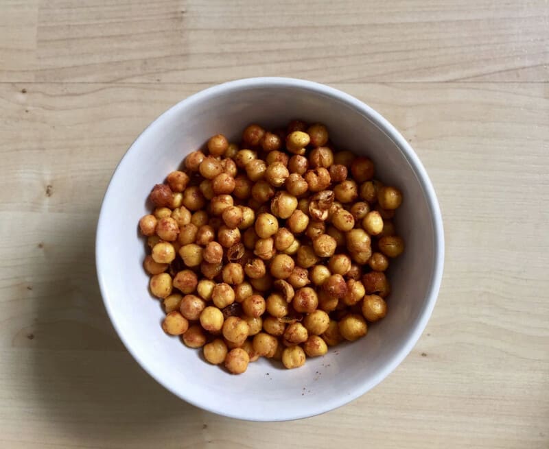 Roasted chickpeas in a white bowl on a wooden table.