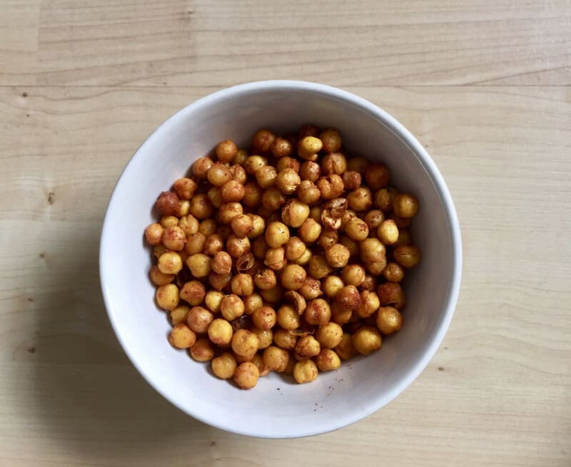 Geroosterde kikkererwten in een witte kom op een houten tafel.