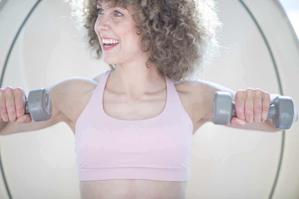 Een vrouw zit in een warmtecabine bij bbb health boutique Amsterdam Jordaan, een holistisch sportschool voor vrouwen. Ze is een workout aan het doen met dumbells.