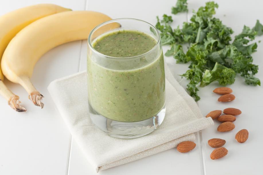 Green smoothie in a glass with kale, banana and almonds.