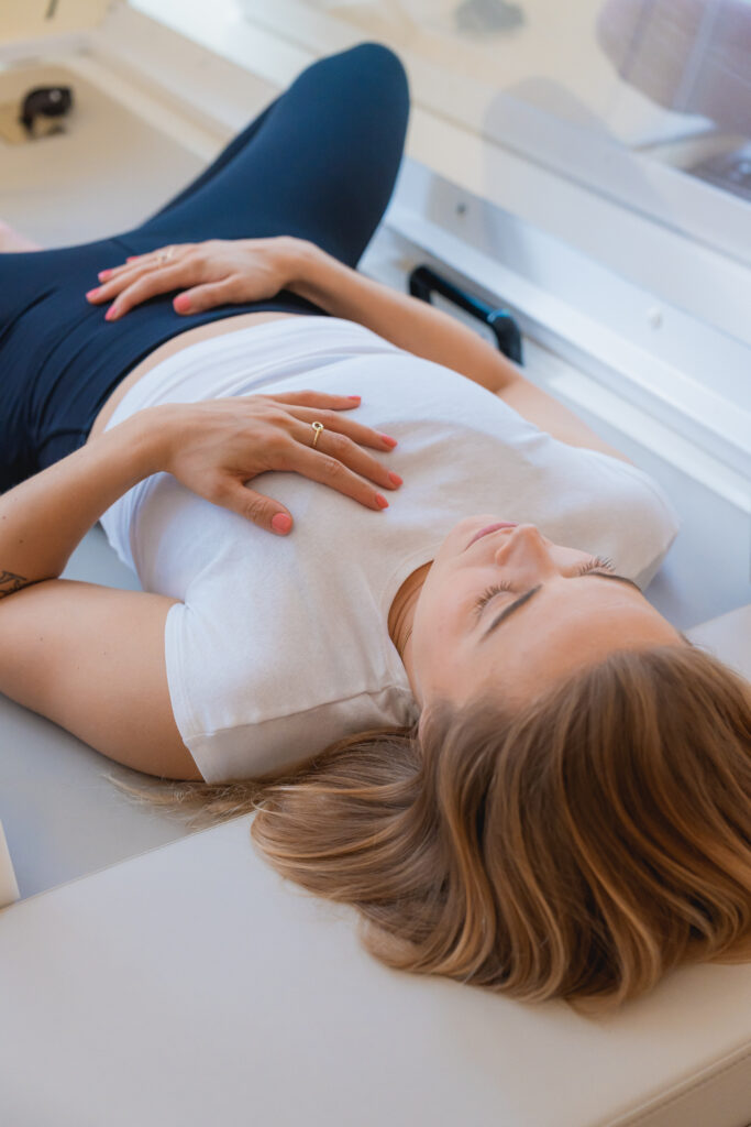 Vrouw ligt in warmtecabine bij bbb health boutique Amsterdam met een hand op haar borst en een hand op haar buik.