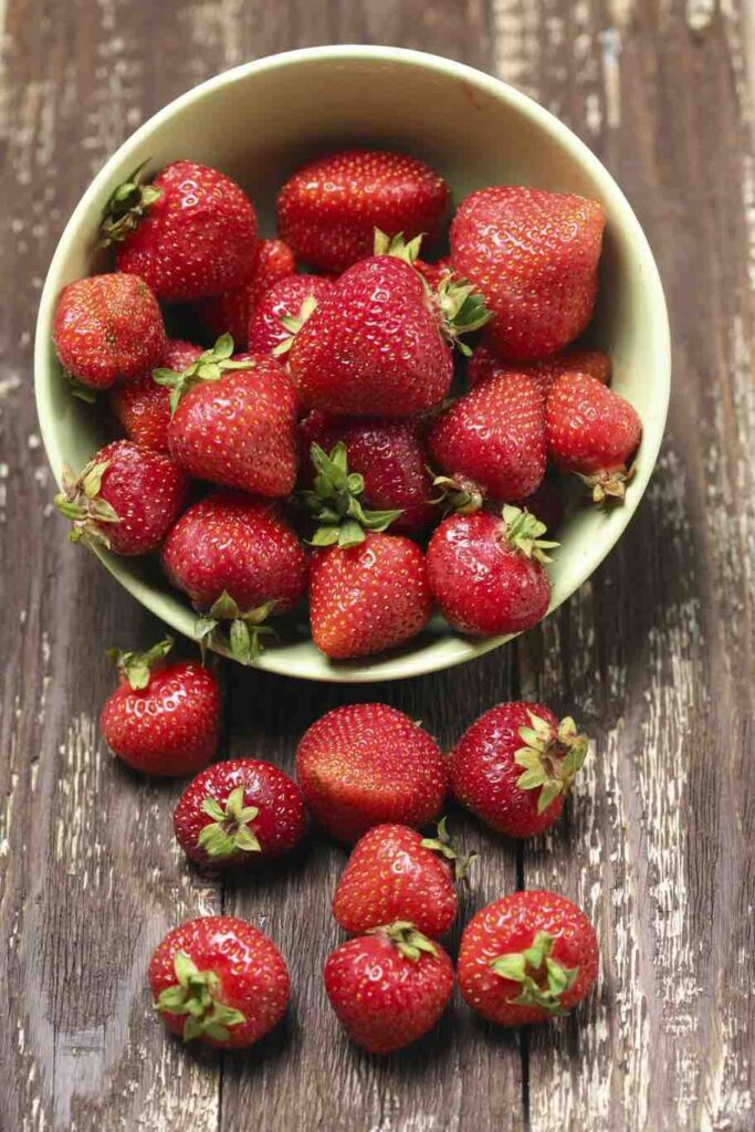 Strawberry in a bowl on wooden table close-up. Vertical image.