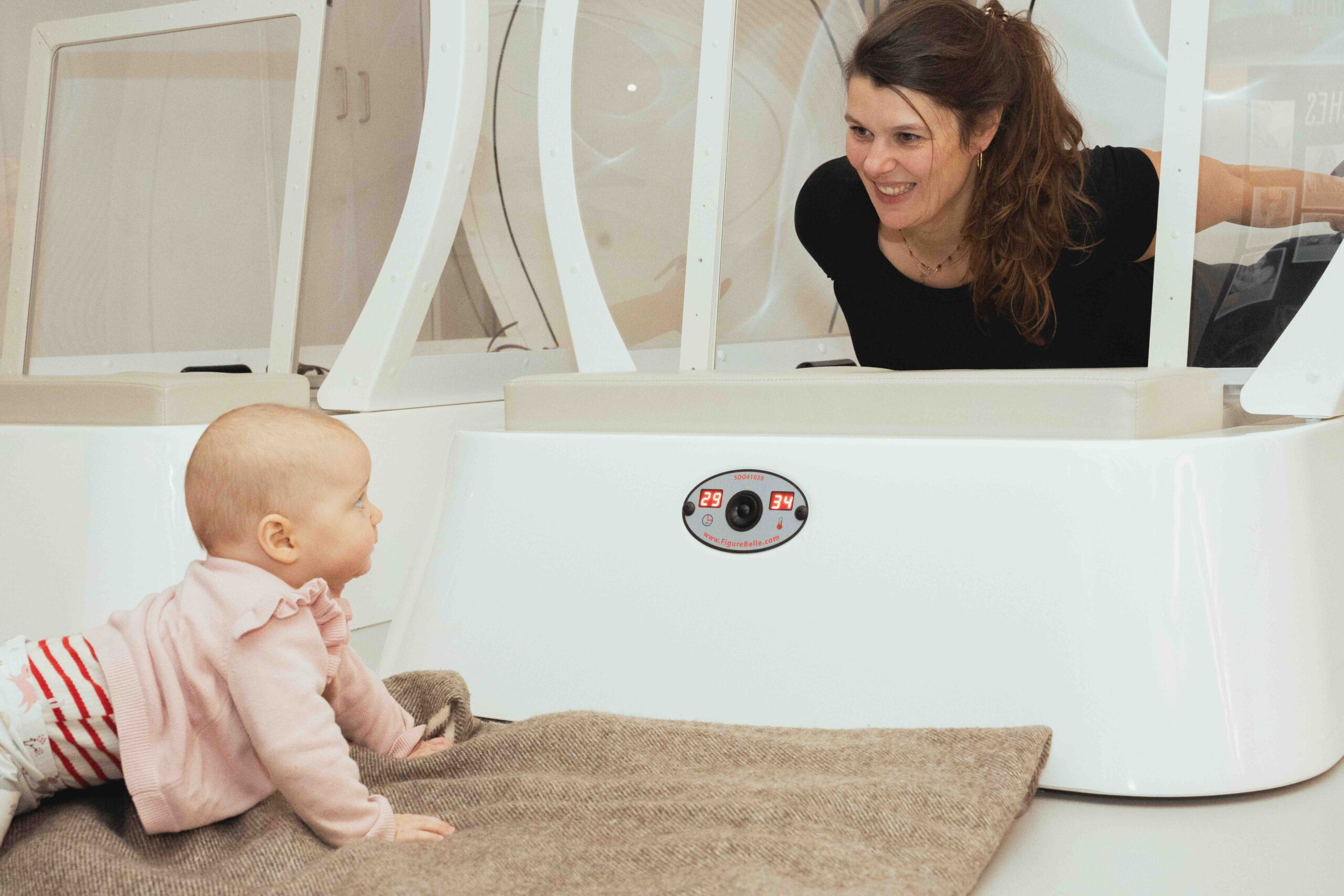 Een baby lacht naar haar moeder die aan het sporten is in de hot cabin bij bbb health boutique Amsterdam Amstel.